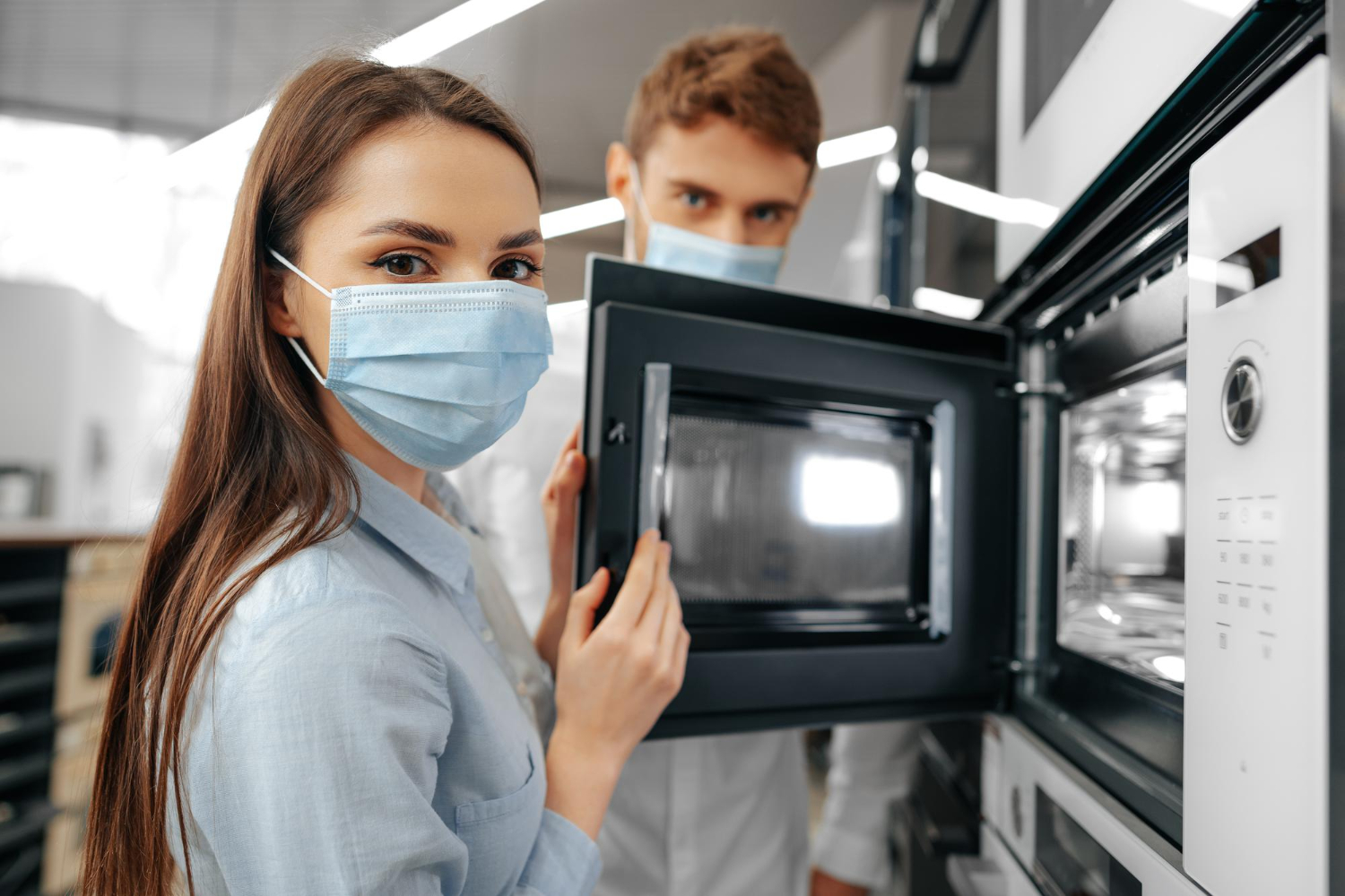 two-people-wearing-face-masks-examining-a-microwave-oven-in-an-appliance-store
